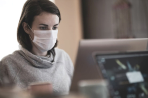 Pandemic worker shortages are felt in this office as a woman works on a computer with a face mask.
