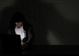 Dark Web Monitoring Services illustrated by a man in a hood searching the dark web.